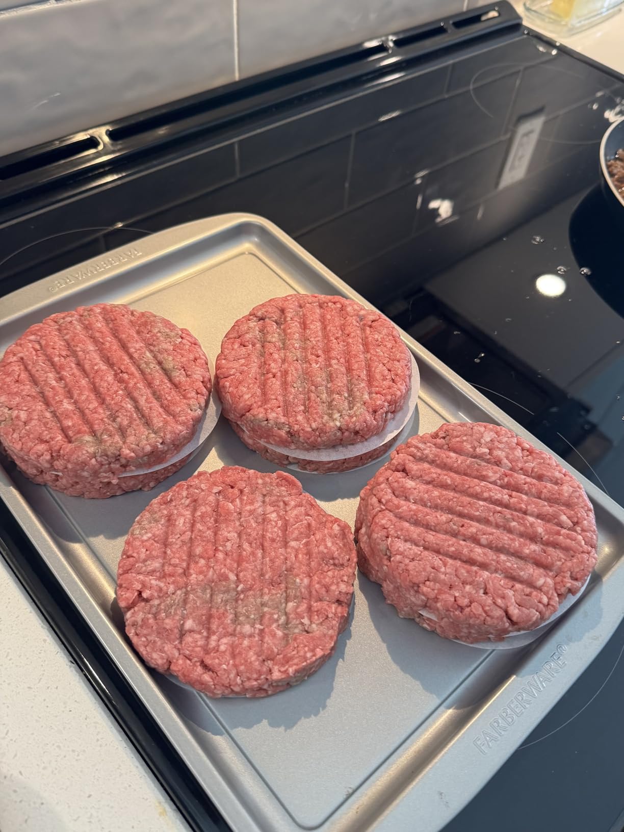 Four evenly pressed burger patties on a metal tray